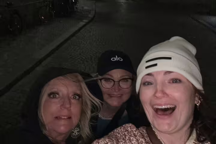 Three smiling women taking a night selfie on a dark cobblestone street in Stockholm