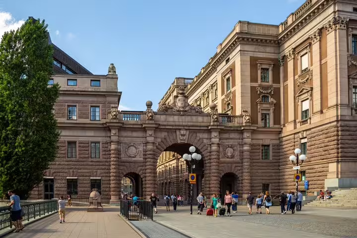 Grand arched gateway of the Swedish Parliament building in Stockholm Old Town with tourists walking nearby