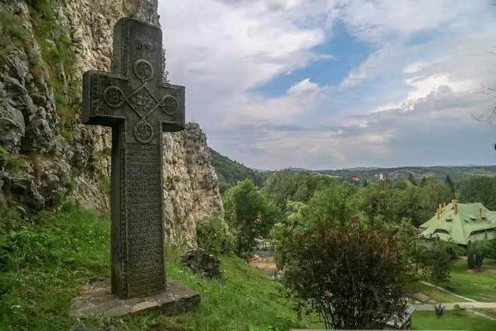 Stone Orthodox cross monument beside rocky cliff with green valley and buildings near Brasov, Romania