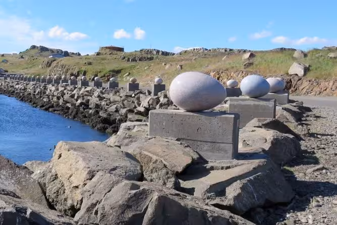 Stone egg sculptures on concrete pedestals along rocky coastline in East Iceland near Hofn
