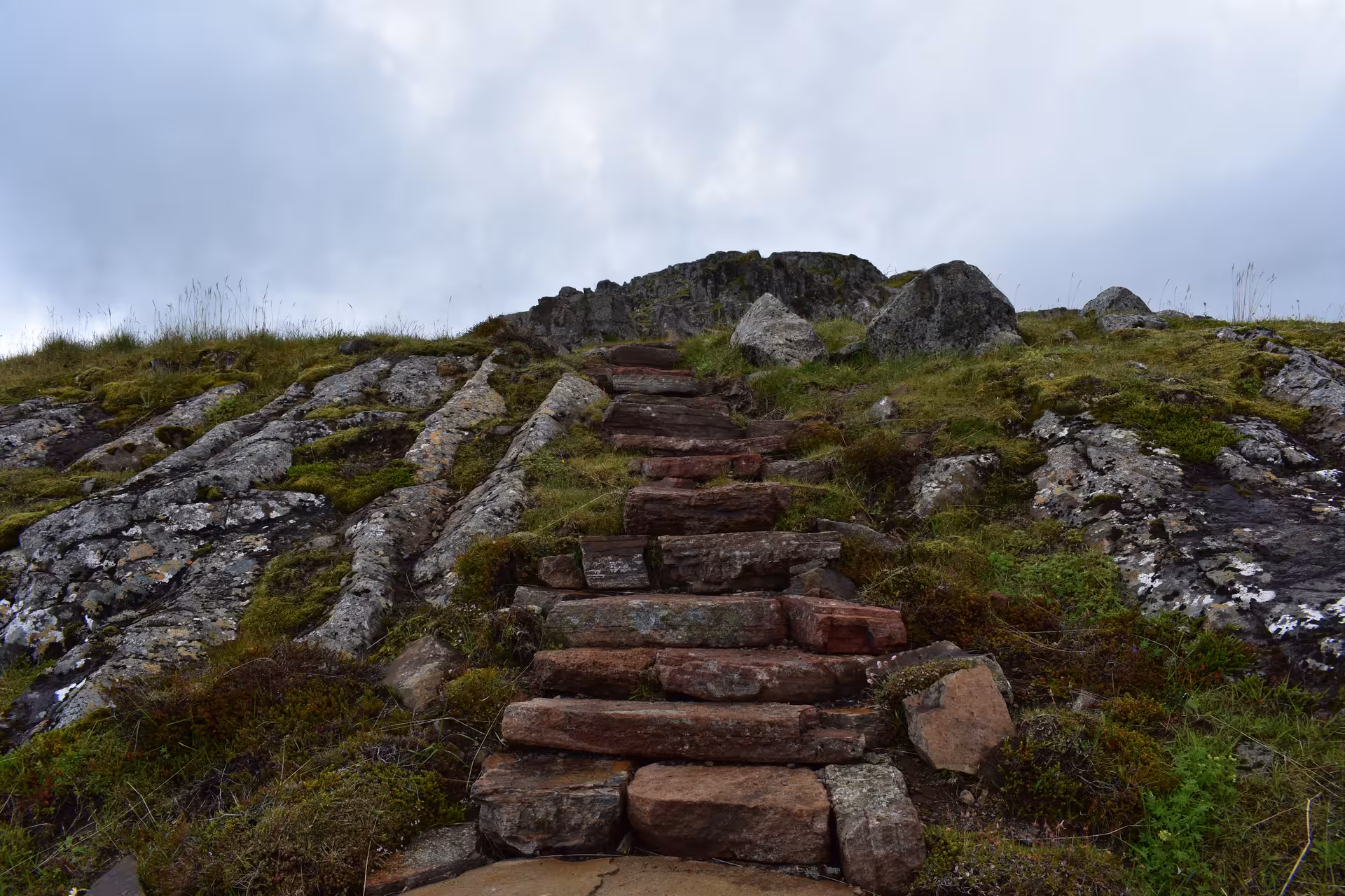 Stone staircase climbing rocky hillside with moss and grass in the Eastfjords of Iceland