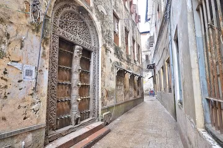 Narrow alley in Stone Town, Zanzibar, showcasing intricate wooden doors and ancient architecture on a walking tour route.