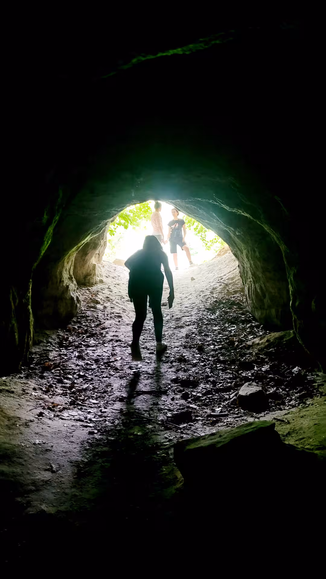 Hikers walking through a dark stone tunnel toward green nature light in Salaj, Romania