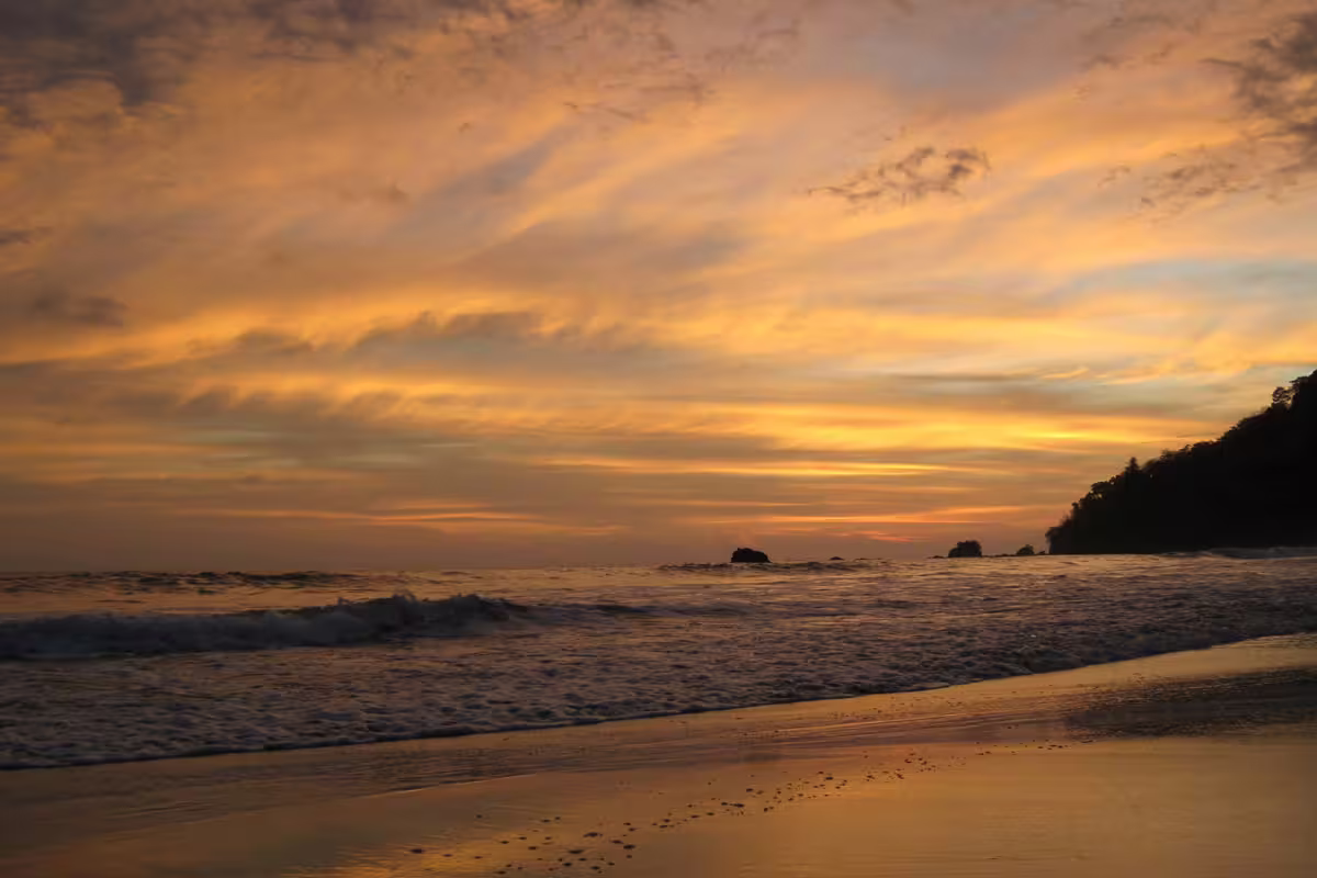Golden sunset over ocean waves on a tropical beach with rocky headland silhouette