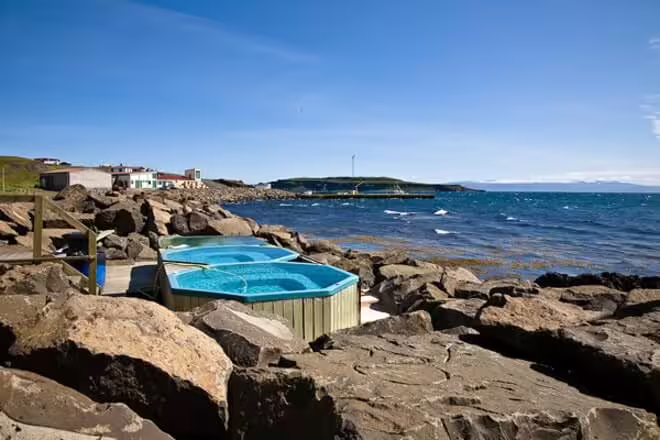 Hot tubs among volcanic rocks on the Strandir coastline in Iceland with blue sea and sky