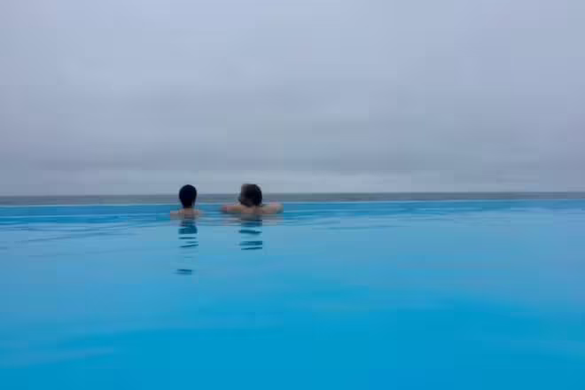 Two people relaxing in an infinity pool overlooking a misty Icelandic coastline