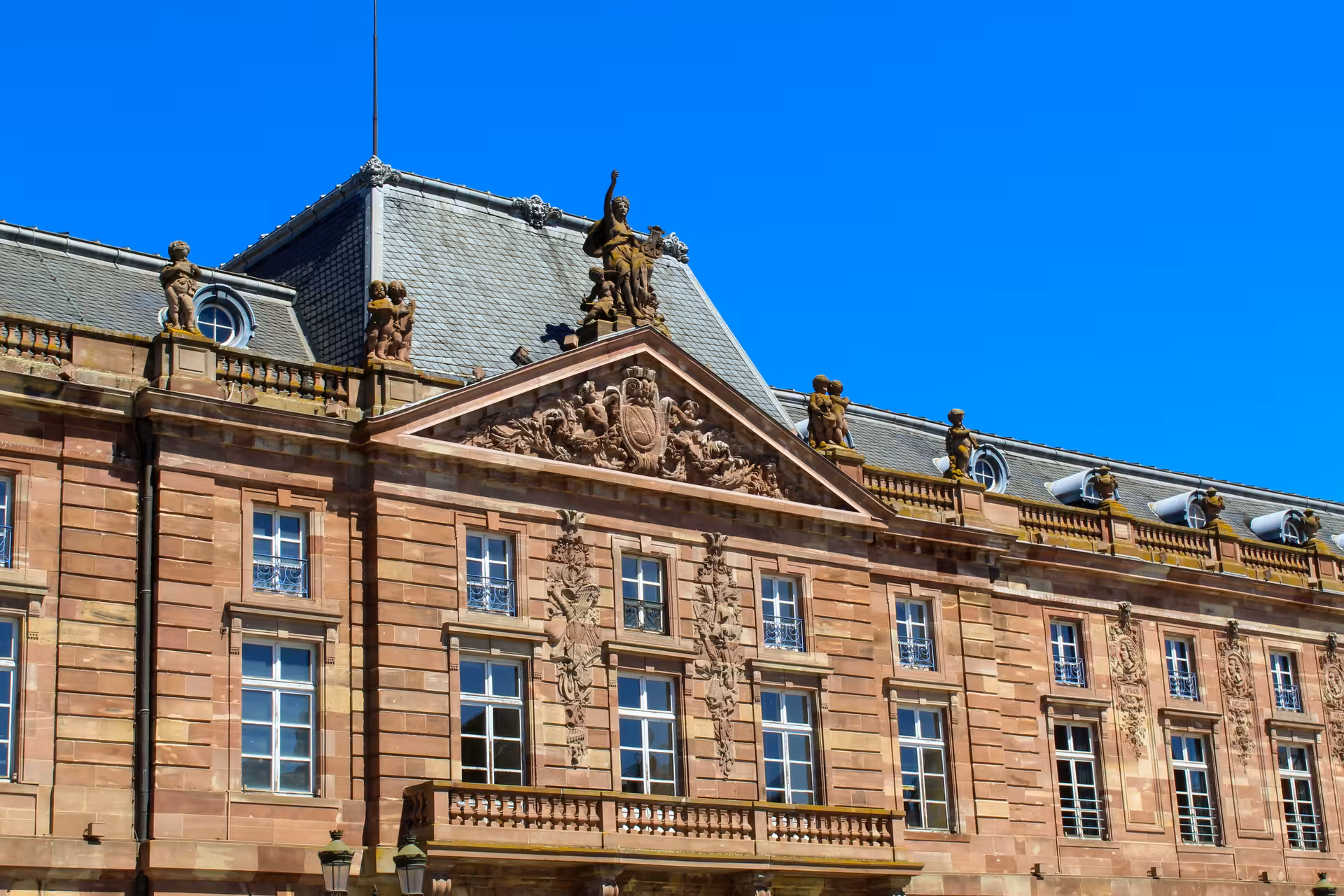 Ornate Baroque facade of a historic Strasbourg sandstone palace with rooftop sculptures under blue sky