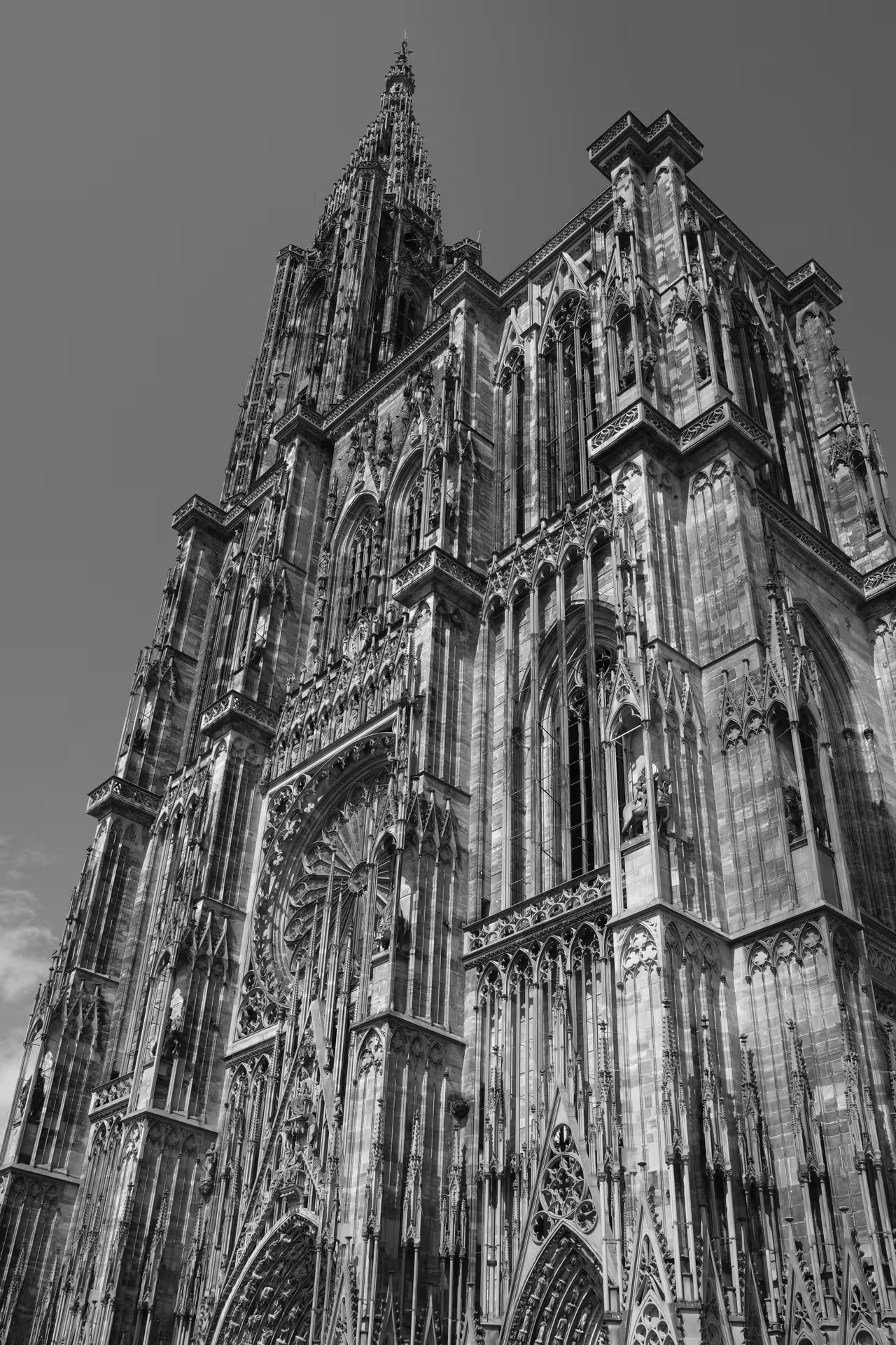 Gothic facade of Strasbourg Cathedral with ornate spire and intricate stone carvings against grey sky