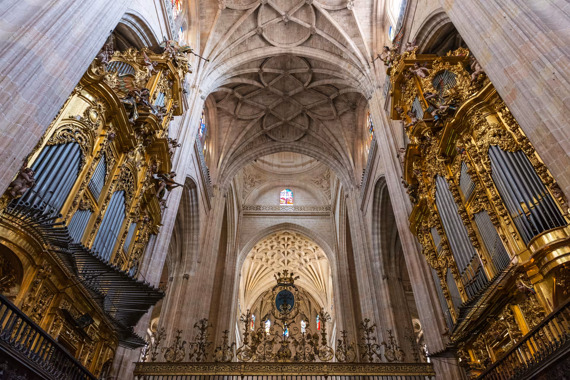 Gothic cathedral interior with ornate golden pipe organs and vaulted stone ceiling
