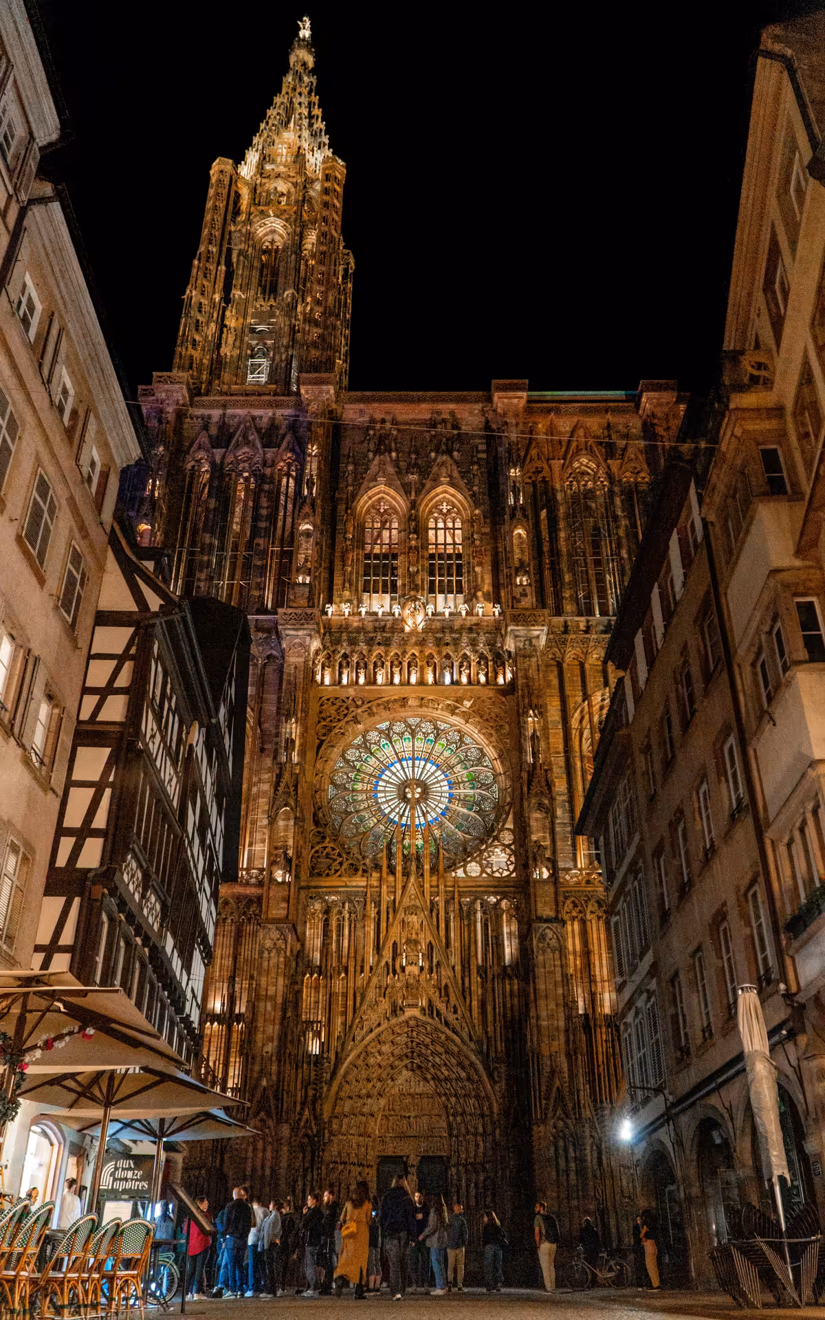 Strasbourg Cathedral illuminated at night with glowing rose window and Gothic spire towering above narrow street