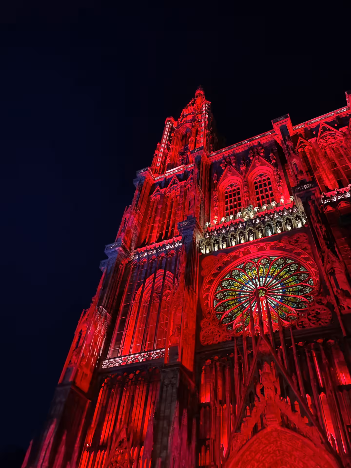 Strasbourg Cathedral illuminated in dramatic red lights at night, showcasing Gothic architecture and rose window