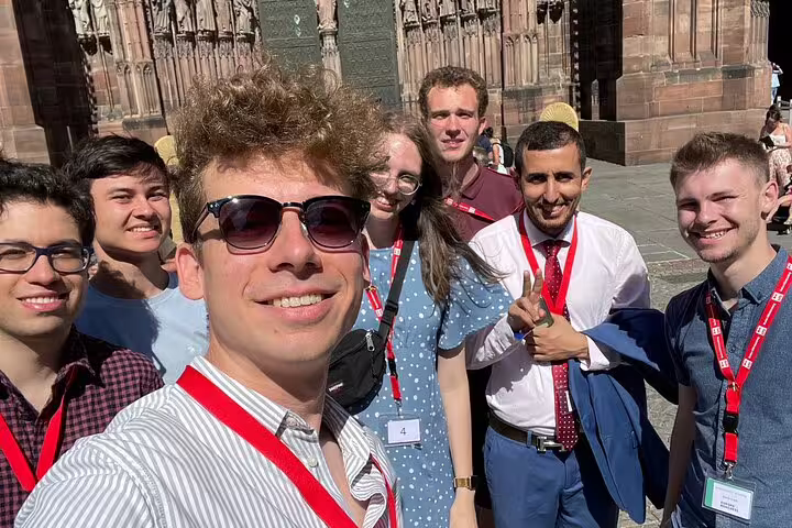Group selfie at Strasbourg Cathedral during a scavenger hunt walking tour, friends wearing lanyards in sunshine