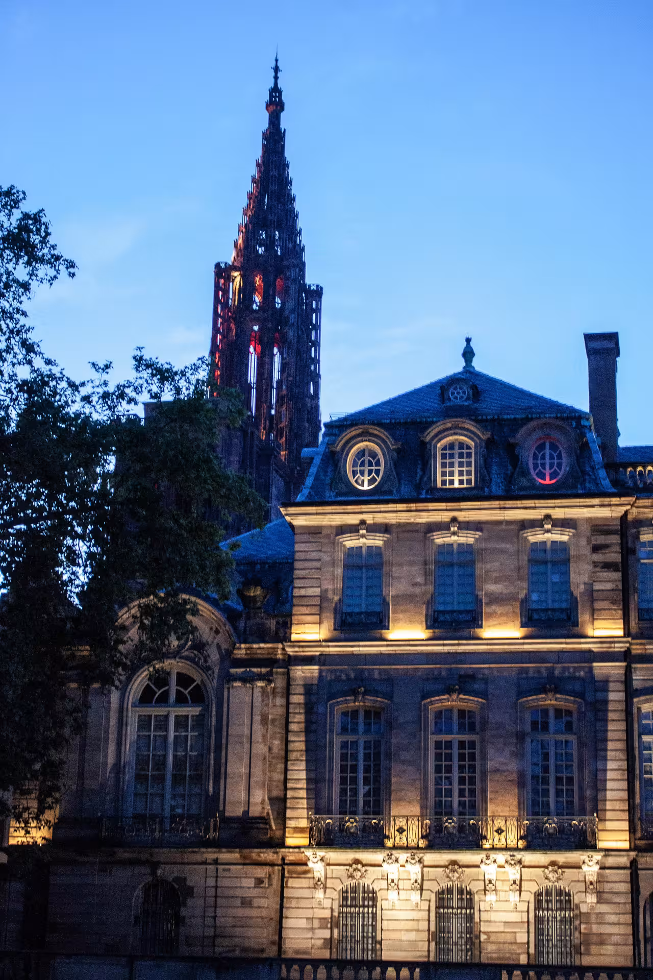 Strasbourg Cathedral spire illuminated at dusk behind a historic mansion with warm lighting