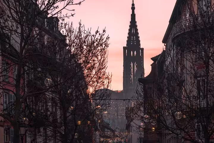 Gothic cathedral spire silhouette at pink sunset over Strasbourg Christmas market street lights