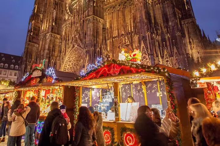 Christmas market stalls with festive lights in front of Strasbourg Cathedral at dusk