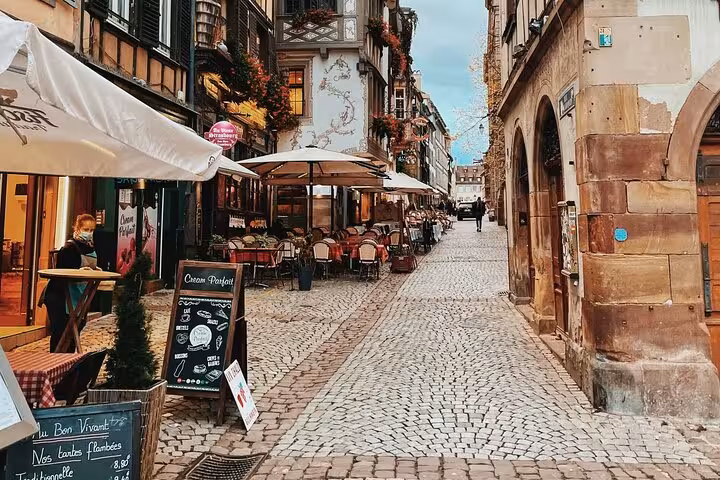 Cobblestone street lined with outdoor restaurant terraces and half-timbered buildings in Strasbourg, France