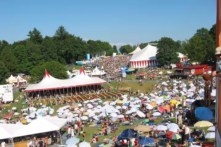 Colorful outdoor festival with large white tents, umbrellas, and crowds on a sunny day in Strasbourg