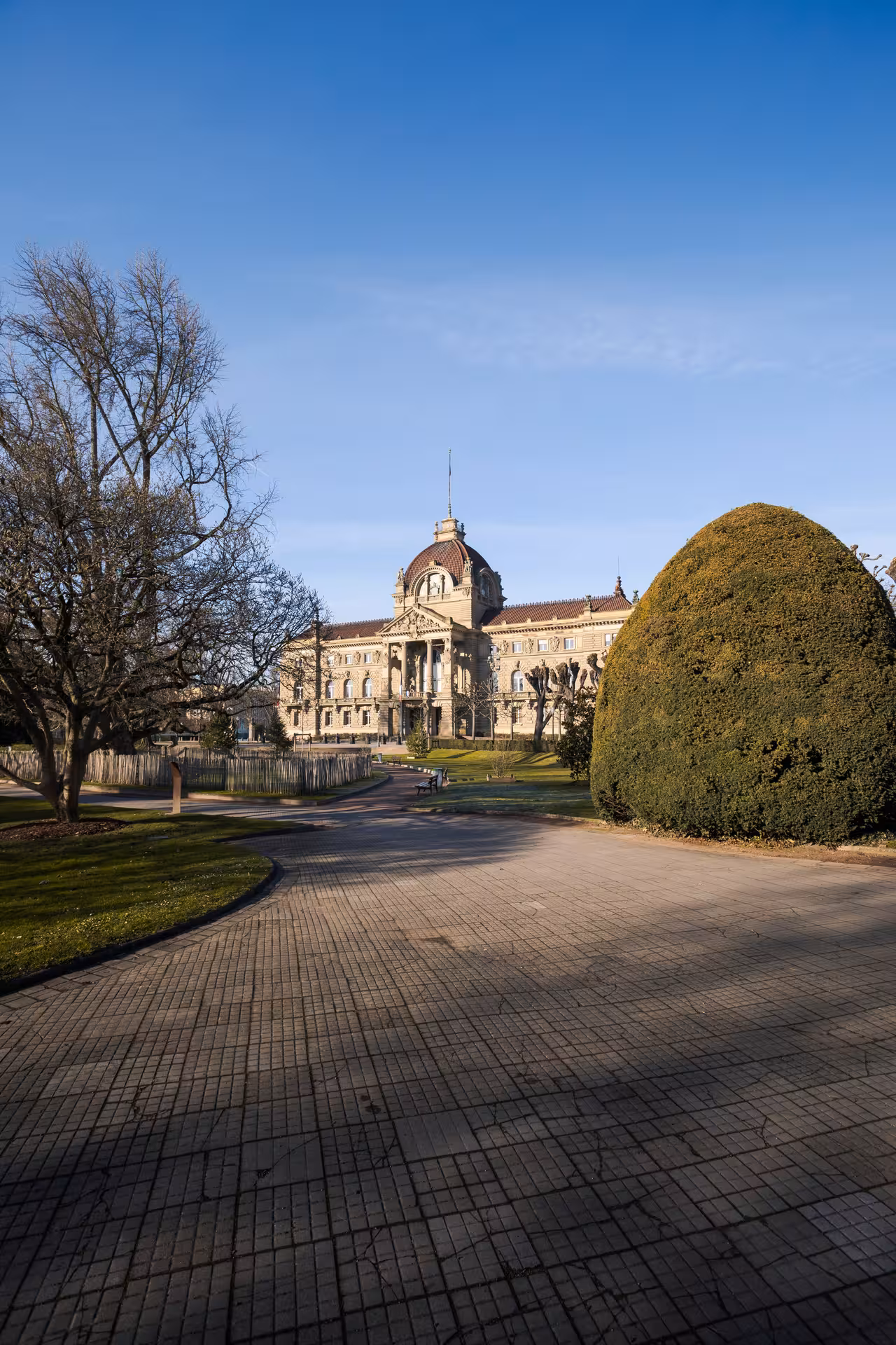 Grand neoclassical building with dome seen from a tree-lined brick pathway in Strasbourg