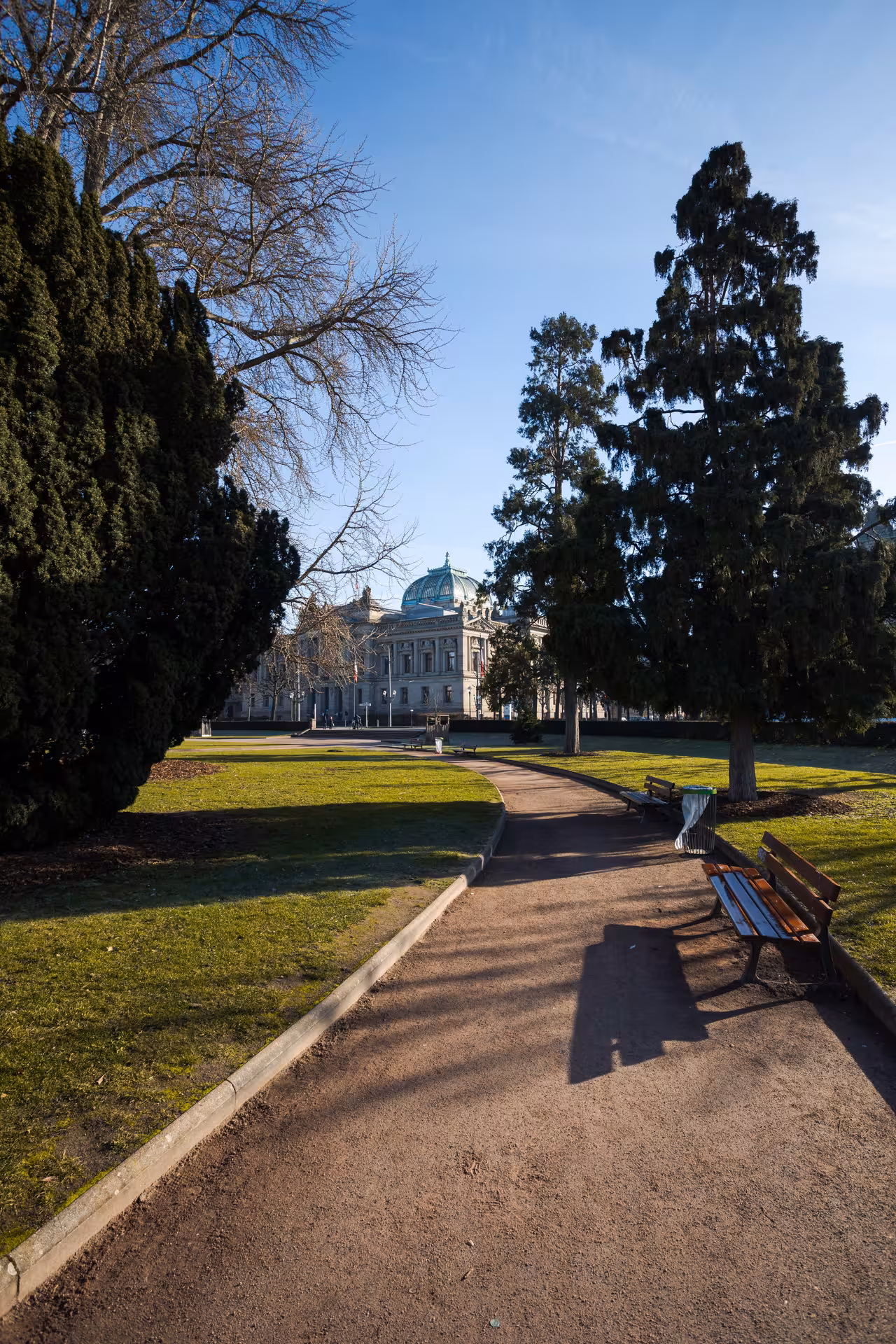 Tree-lined park path leading to a neoclassical domed building in Strasbourg on a sunny day
