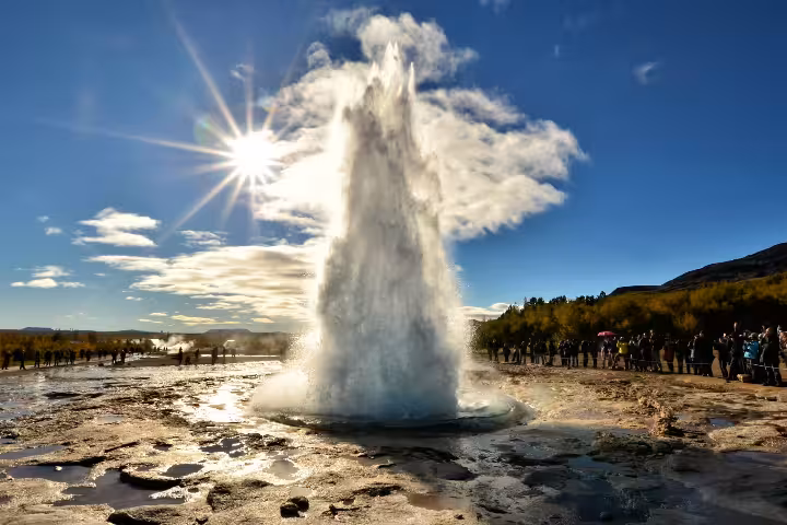 Strokkur geyser erupting on Iceland's Golden Circle with tourists watching under a sunny blue sky