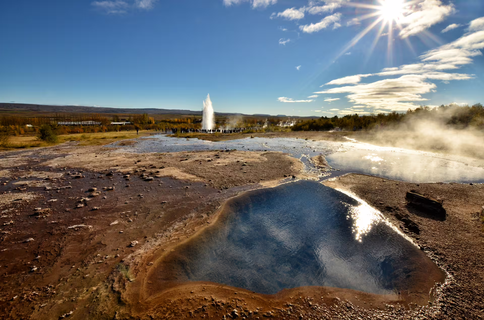 Strokkur geyser erupting at Geysir geothermal area with hot spring pool in foreground, Golden Circle Iceland