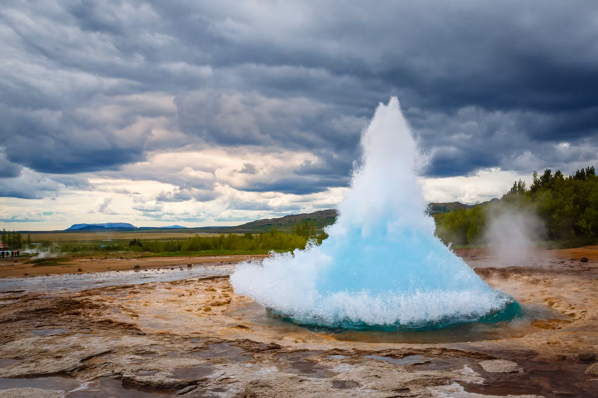Strokkur geyser erupting with vivid blue water on Iceland's Golden Circle under dramatic cloudy skies