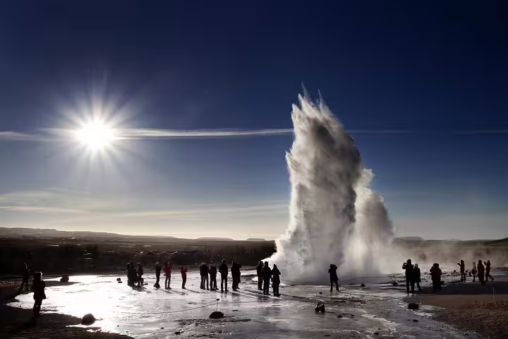 Tourists watching Strokkur geyser eruption on Iceland's Golden Circle tour under bright sunlight