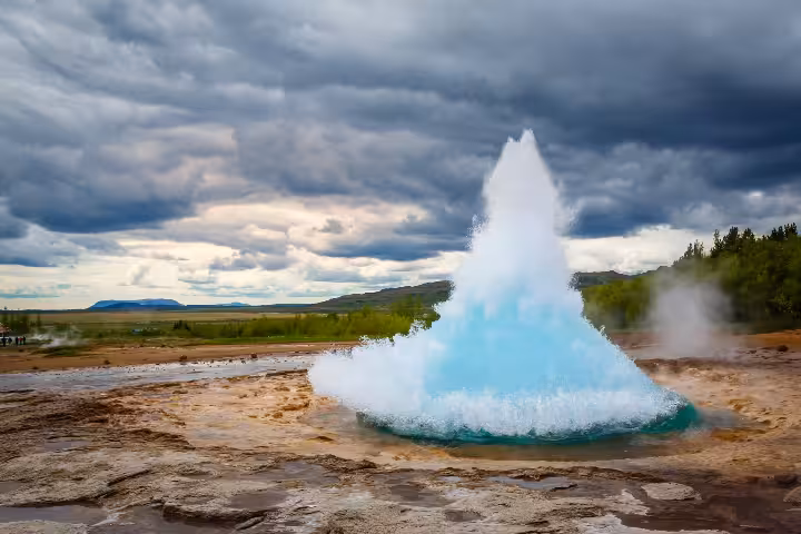 Strokkur geyser erupting with turquoise water bubble in Iceland's Golden Circle under dramatic cloudy sky