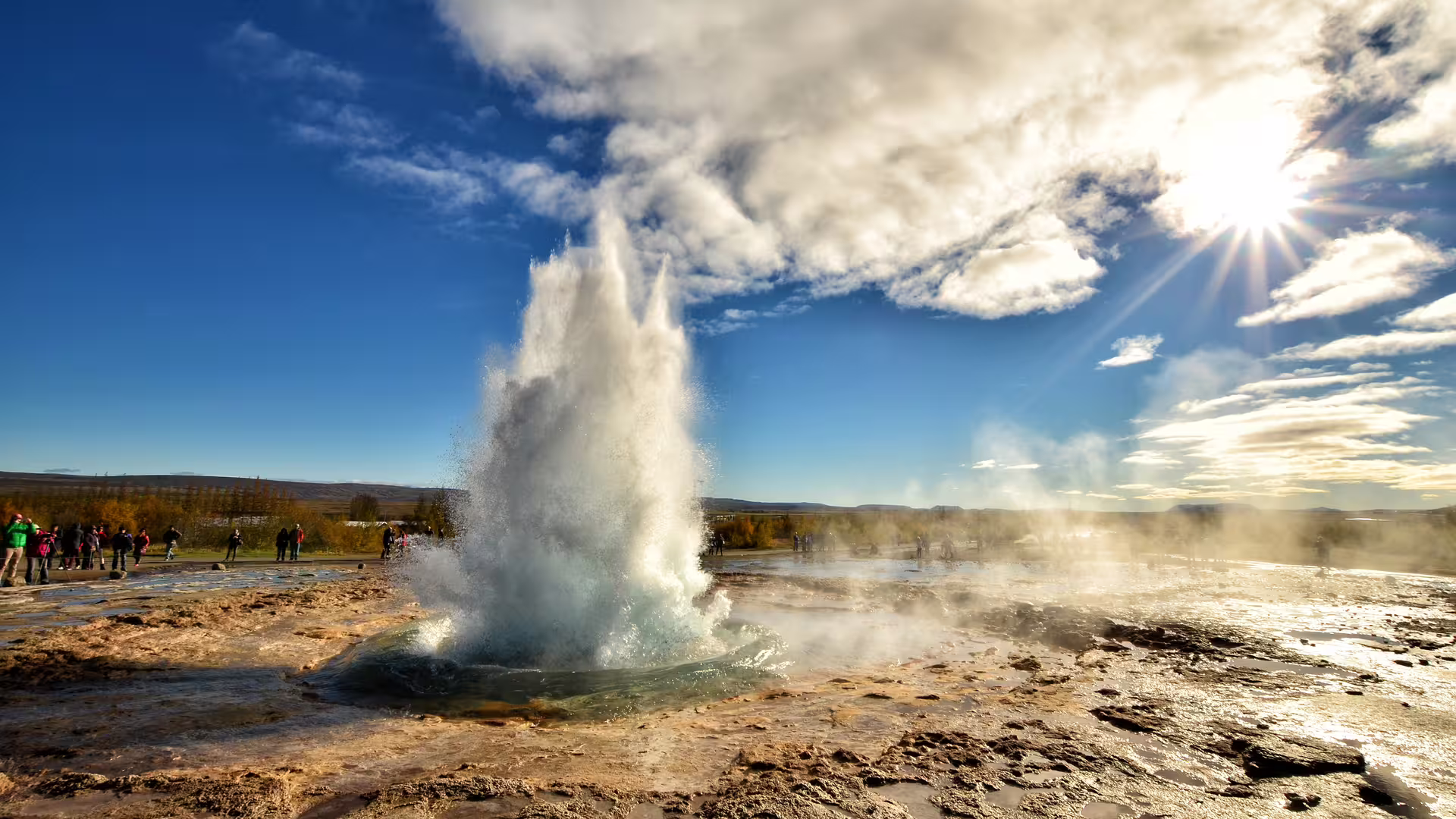 Strokkur geyser erupting on Iceland's Golden Circle with tourists watching under blue sky
