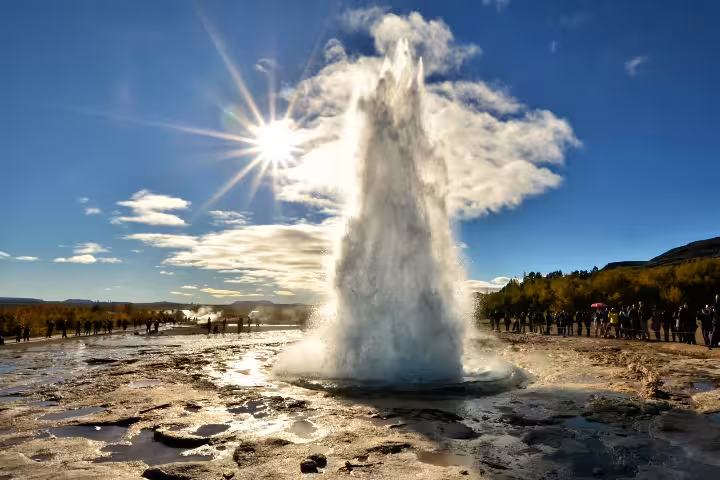 Strokkur geyser erupting on Iceland's Golden Circle with crowds of tourists watching under blue sky