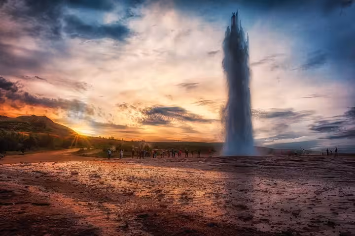 Strokkur geyser erupting at sunset on Iceland's Golden Circle with tourists watching nearby