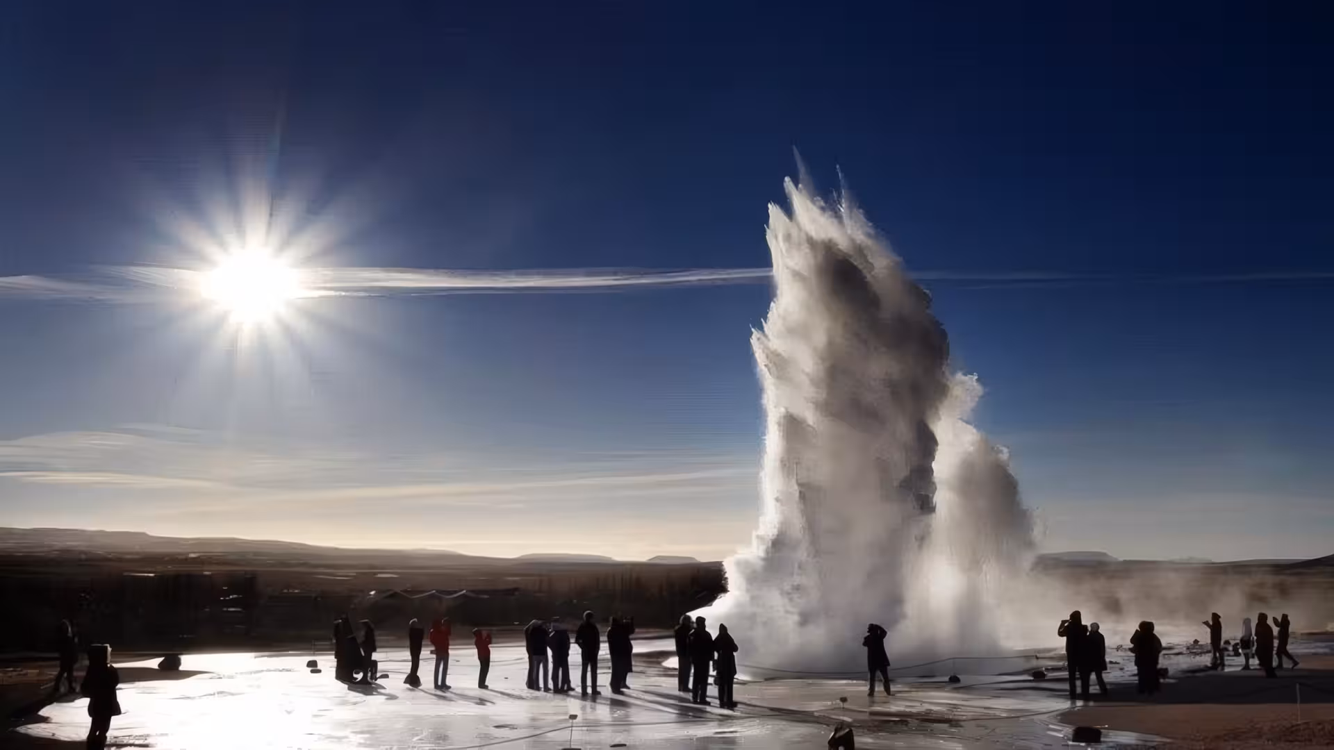Strokkur geyser erupting on Iceland's Golden Circle with tourists watching under a clear blue sky