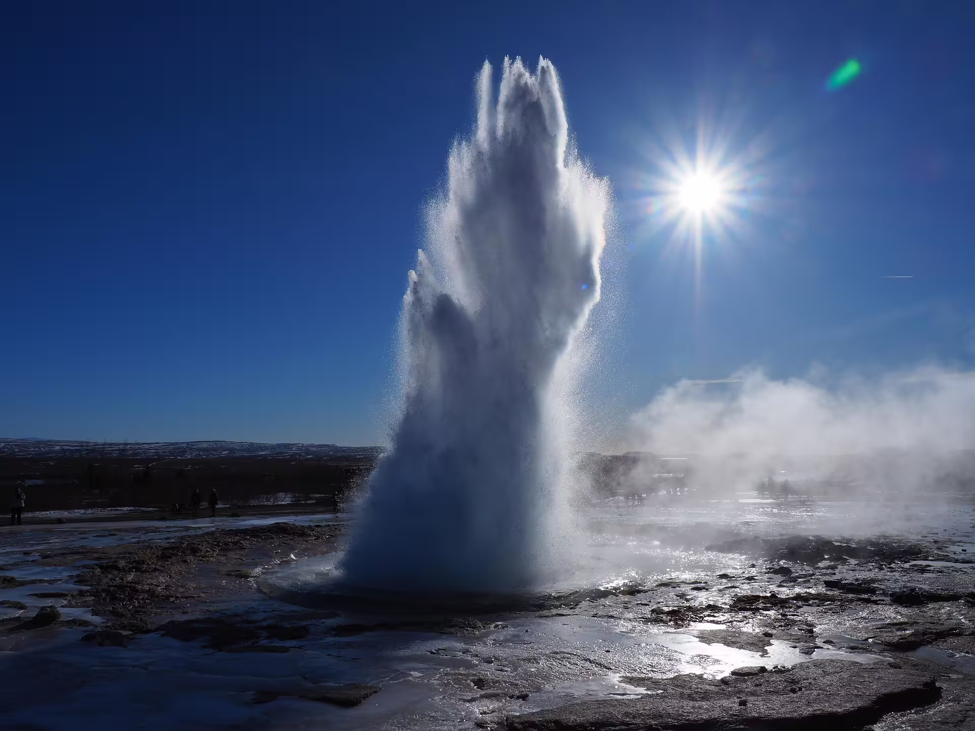 Strokkur geyser erupting on Iceland's Golden Circle under bright blue sky and sunlight