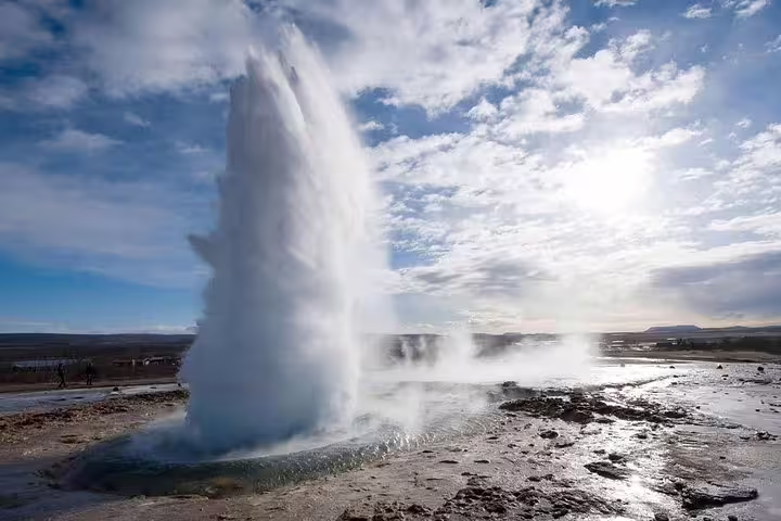 Strokkur geyser erupting on Iceland's Golden Circle with steam rising against a cloudy sky