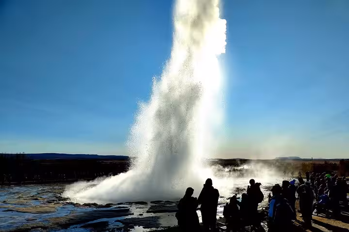 Strokkur geyser erupting on Iceland's Golden Circle with tourists watching against a clear blue sky