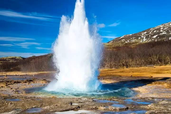 Strokkur geyser erupting on Iceland's Golden Circle with snow-capped mountains in the background