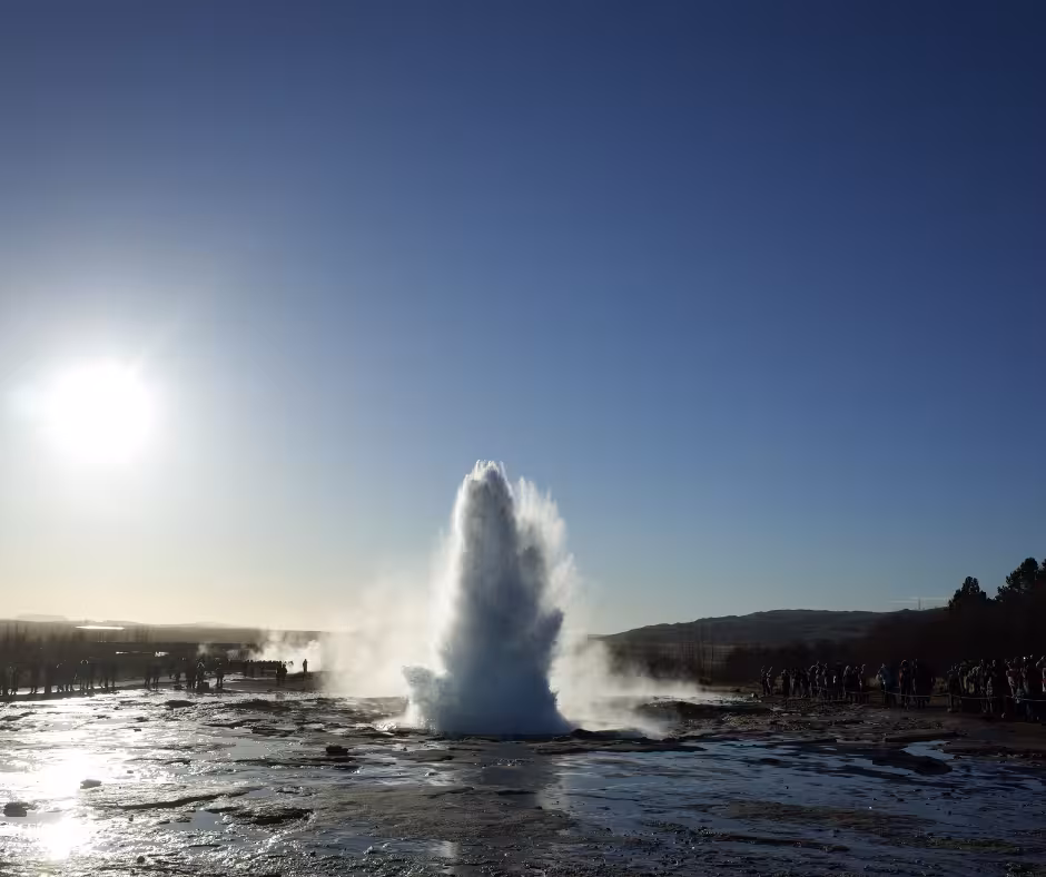 Strokkur geyser erupting on Iceland's Golden Circle with tourists watching under a clear blue sky