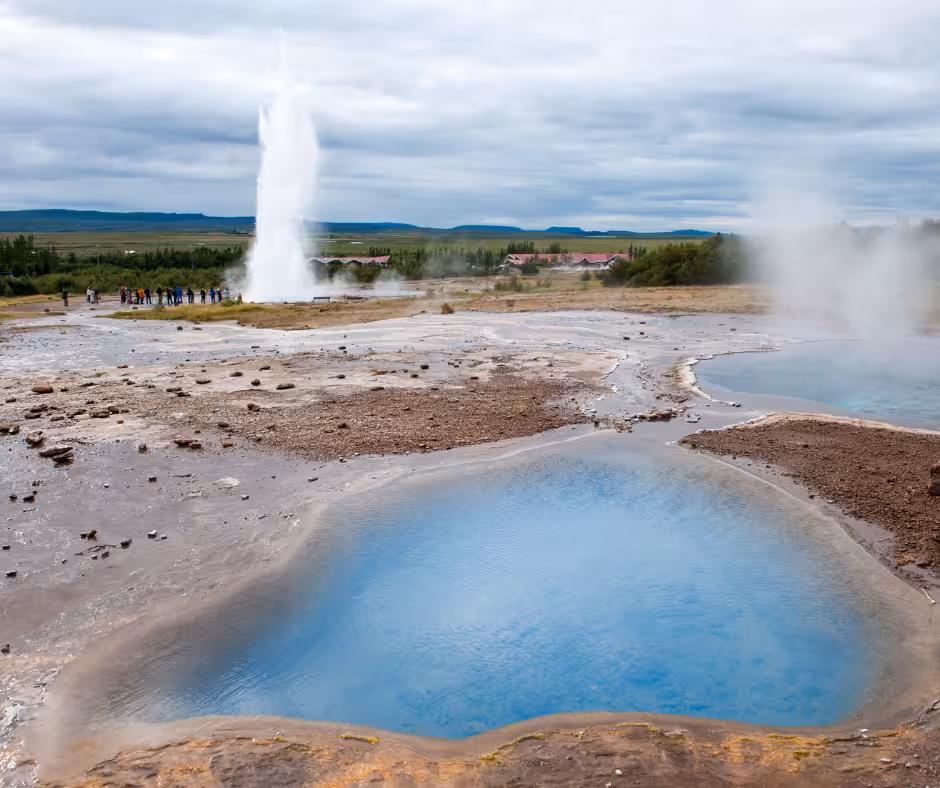 Strokkur geyser erupting at Geysir geothermal area with blue hot spring pool in foreground, Iceland