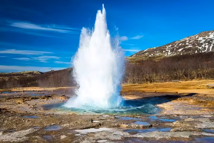 Strokkur geyser erupting on Iceland's Golden Circle route with snow-capped mountains in background