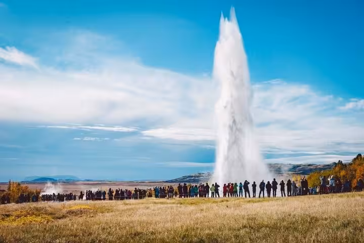 Crowds watching Strokkur geyser eruption on Iceland's Golden Circle tour under blue sky