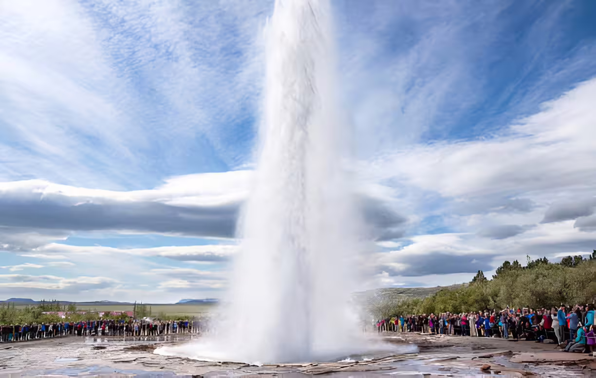 Strokkur geyser erupting high into sky with crowds of tourists watching at Golden Circle Iceland