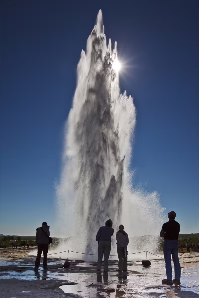 Tourists watching Strokkur geyser eruption on Iceland's Golden Circle tour under clear blue sky