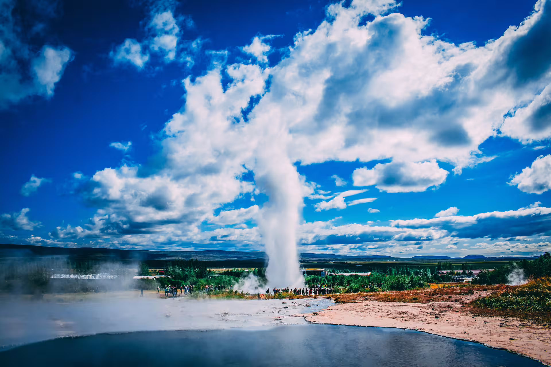 Strokkur geyser erupting on Iceland's Golden Circle with tourists watching and blue sky backdrop