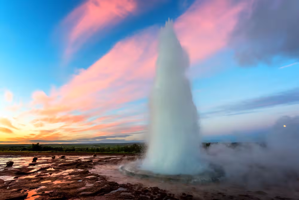 Strokkur geyser erupting at sunset with pink clouds during Iceland Golden Circle tour
