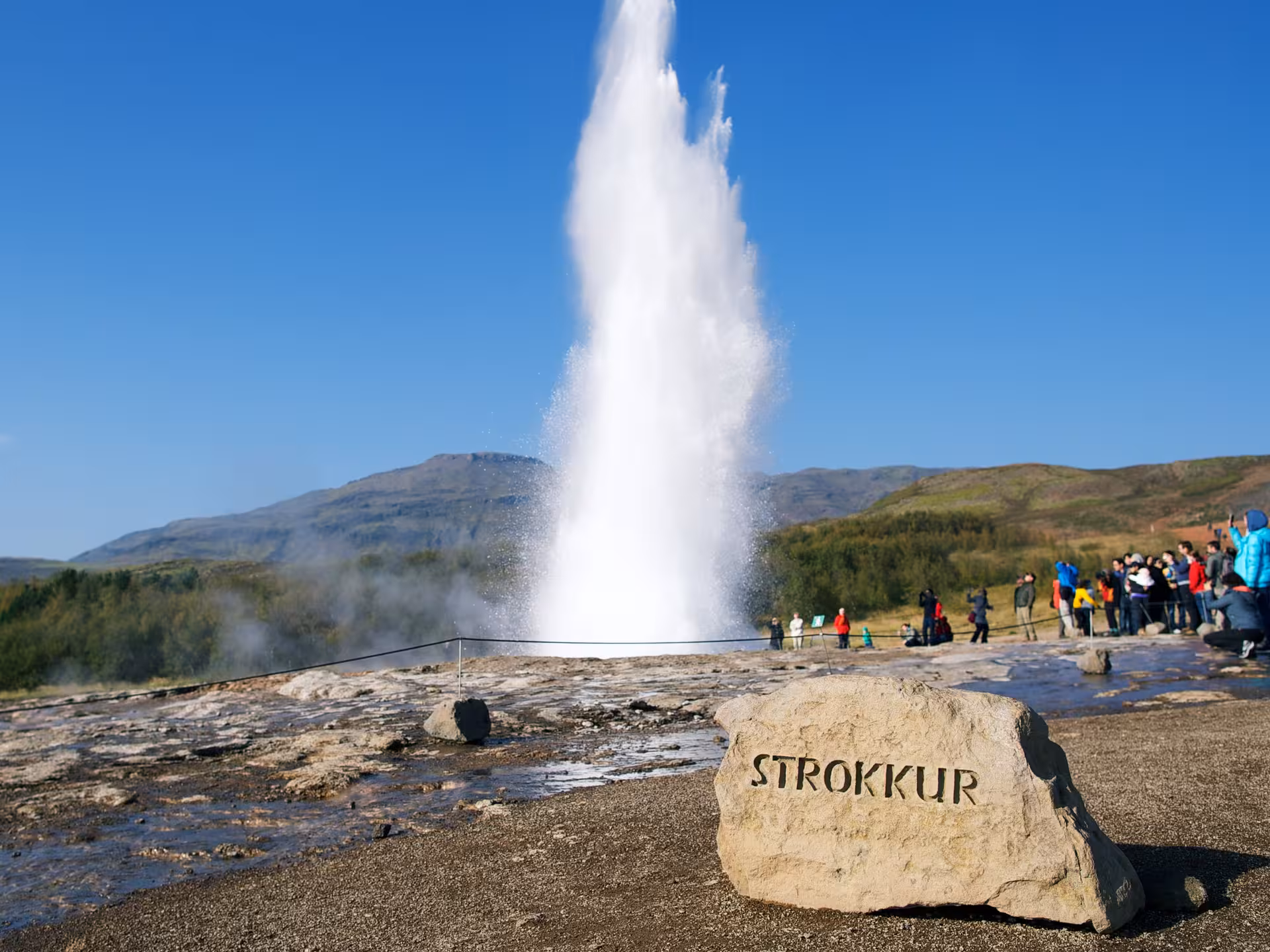 Strokkur geyser erupting in Iceland under a clear blue sky, a highlight of the Northern Lights Hunt tour.