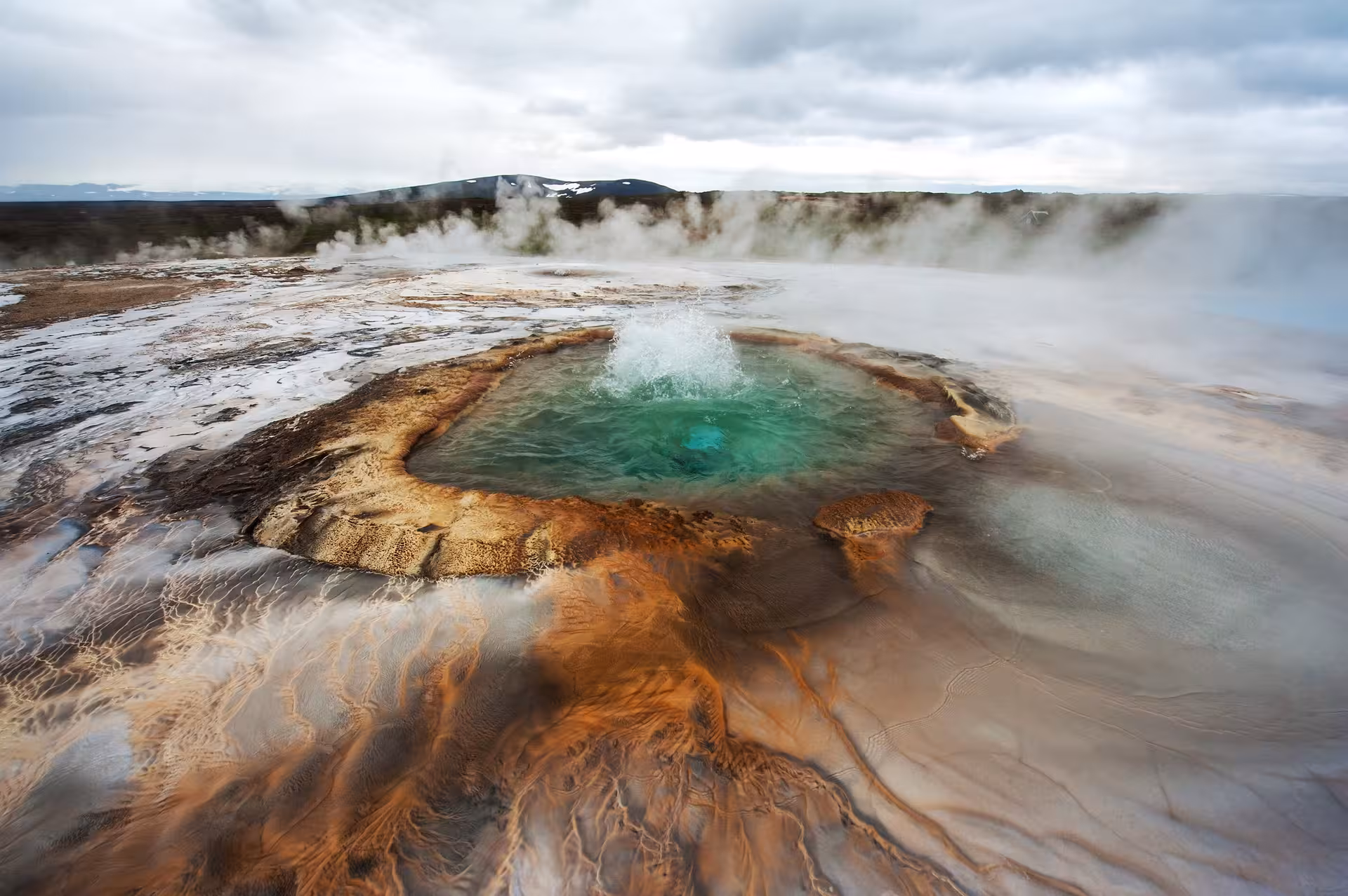 Explosive geothermal activity at Iceland's Strokkur Geysir, showcasing vibrant mineral deposits and steam.