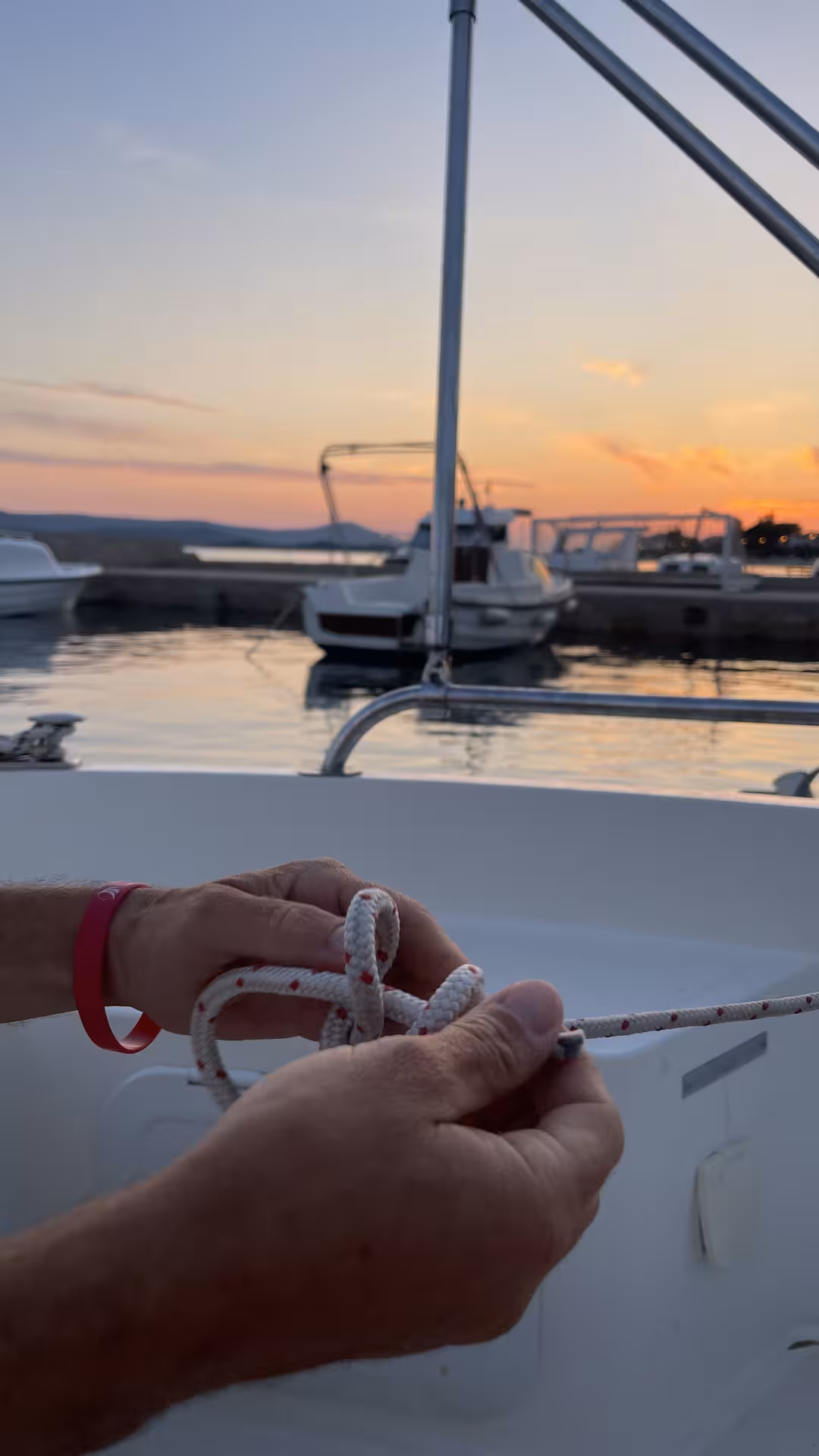 Student tying sailing knot on deck at sunset marina, practical “Zero to hero” skipper training session