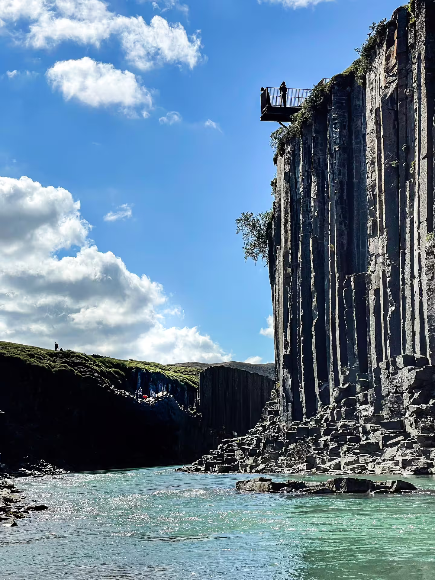 Towering basalt column cliffs of Studlagil Canyon with viewing platform and turquoise glacial river below