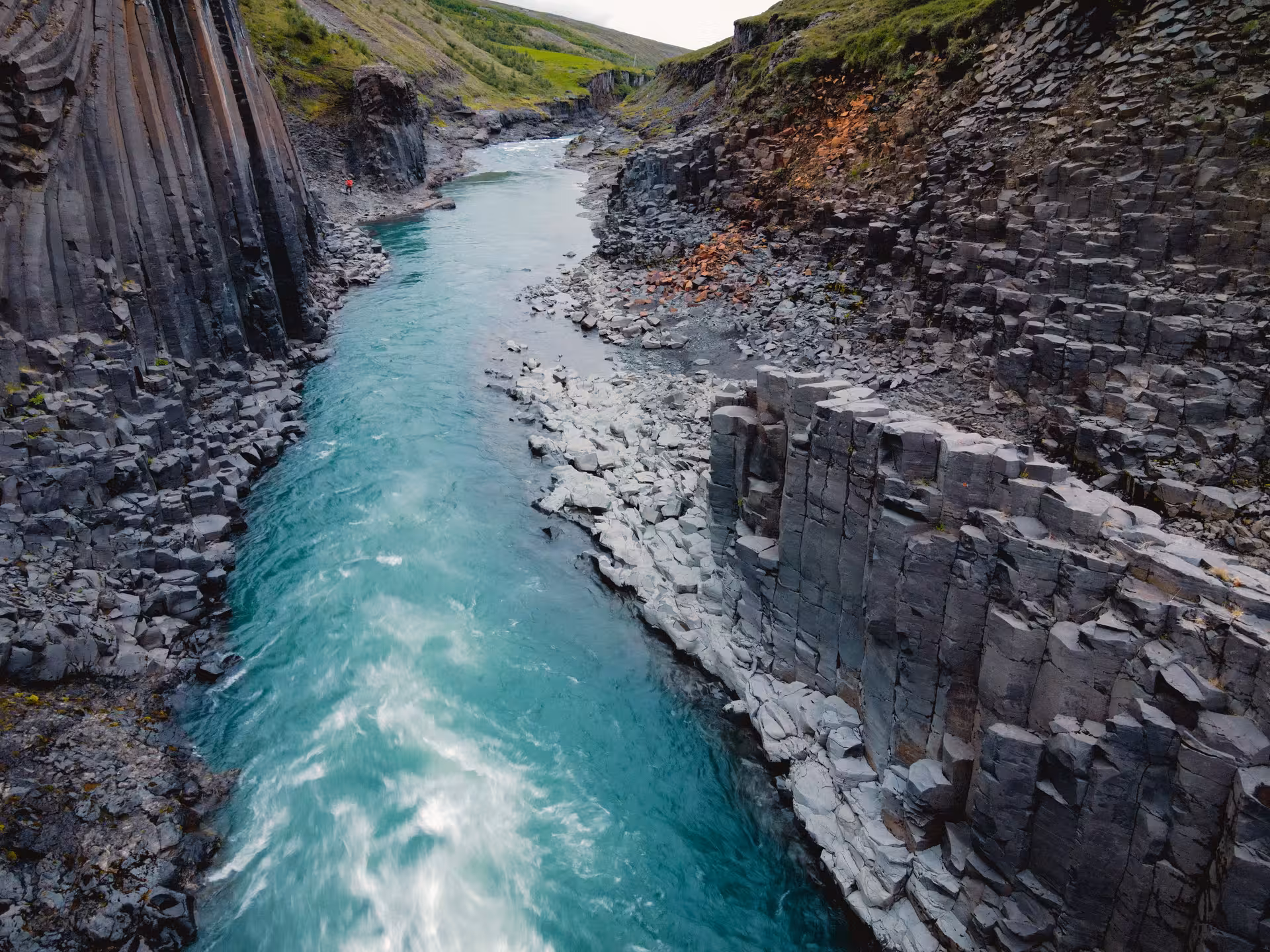 Turquoise glacial river flowing through Studlagil Canyon's dramatic basalt column walls in Iceland