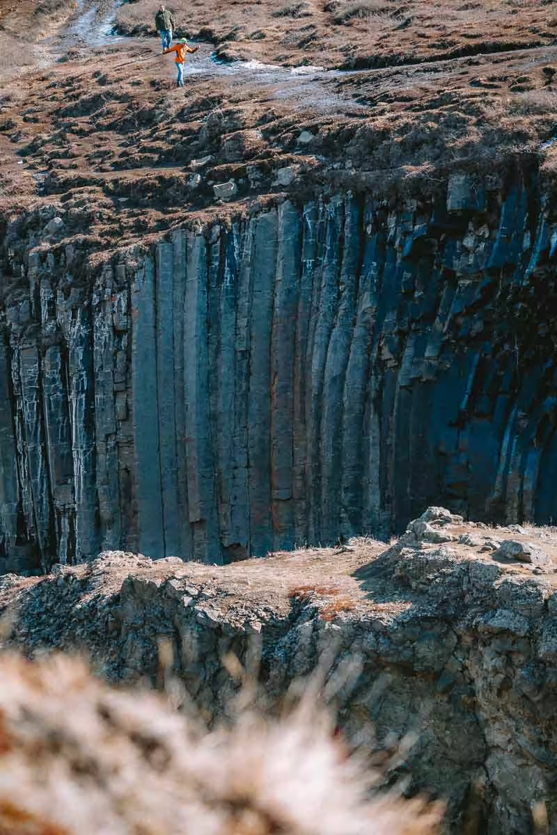 Towering basalt column walls of Studlagil Canyon with two hikers standing at the rim edge